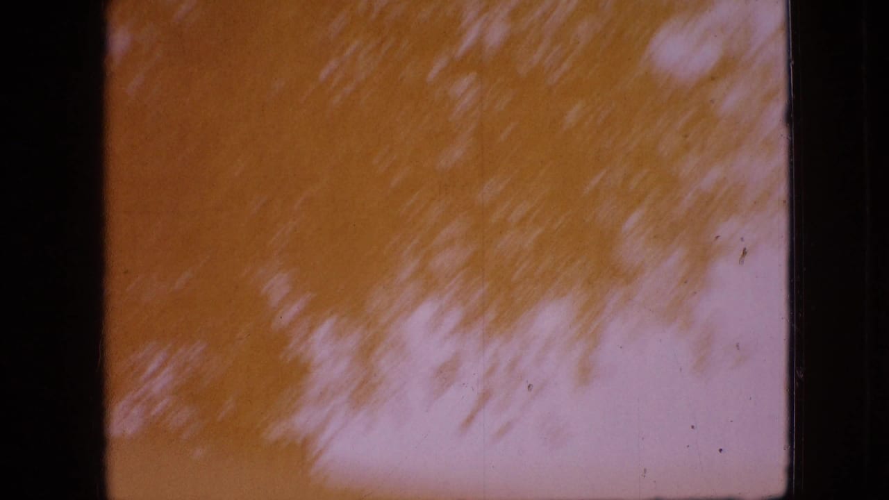 1968 Branson, Missouri 8mm frame with orange color shift, soft tree-shadow shapes, pale sky, and dark film edges.