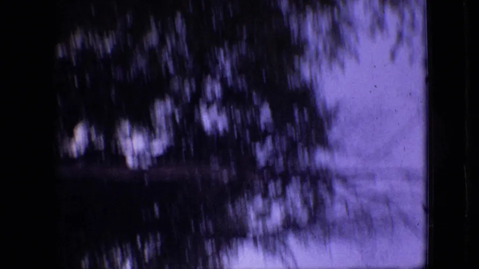 1968 Branson, Missouri home-movie frame showing silhouetted foliage, purple-blue sky, and a faint exterior structure at the edge of the shot.