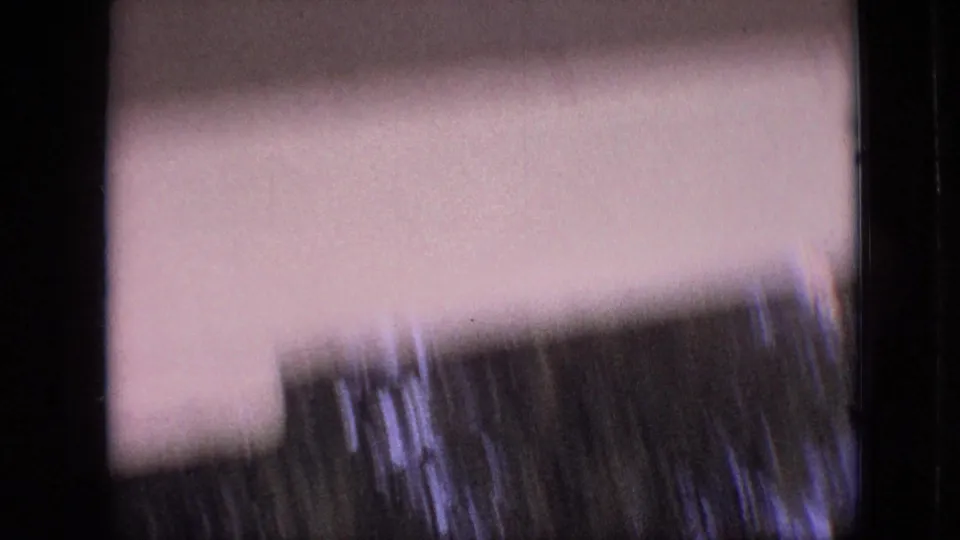 1968 Branson, Missouri home-movie frame with a blurred light-toned building surface, dark foliage, and motion-softened film texture.