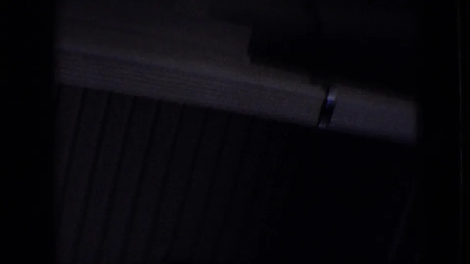 Dark handheld 8mm frame showing a shadowed interior or window area with a pale horizontal bar and indistinct vertical surfaces.