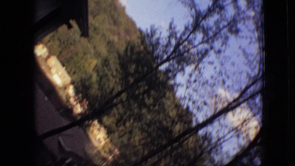 Tilted 1968 Branson home-movie view of leafy trees, blue sky, hillside vegetation, and dark window or frame edges in the foreground.