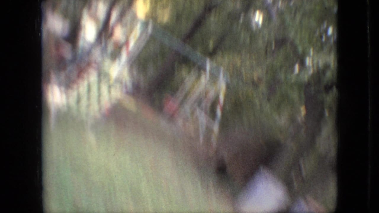 A motion-blurred 1968 8mm home-movie frame from Branson, Missouri, showing a green yard, trees, and soft streaks of foliage within dark film borders.