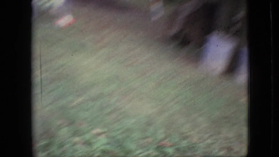 Fast handheld 8mm frame showing blurred green lawn, dark indistinct shapes, and film-frame edges during a rapid move across the backyard.