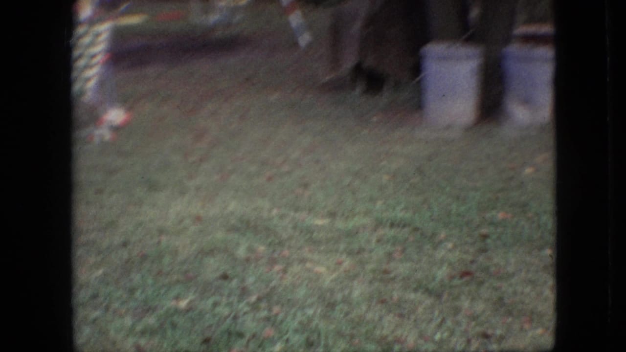 1968 Branson, Missouri 8mm frame showing a soft, handheld view of grass with a patterned outdoor chair and pale cylindrical containers at the edge of the yard.