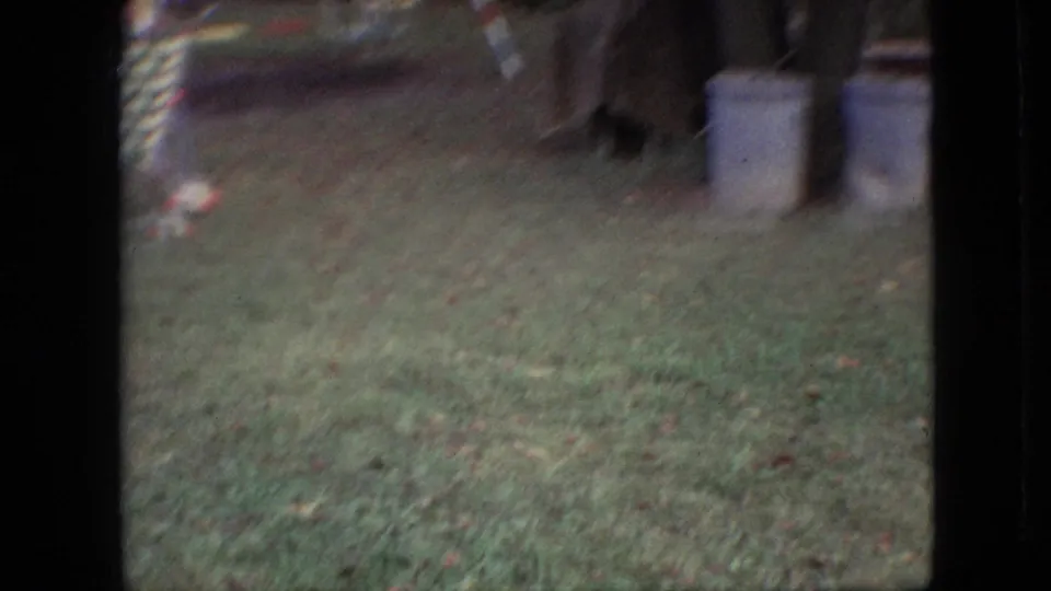 1968 Branson, Missouri 8mm frame showing a soft, handheld view of grass with a patterned outdoor chair and pale cylindrical containers at the edge of the yard.