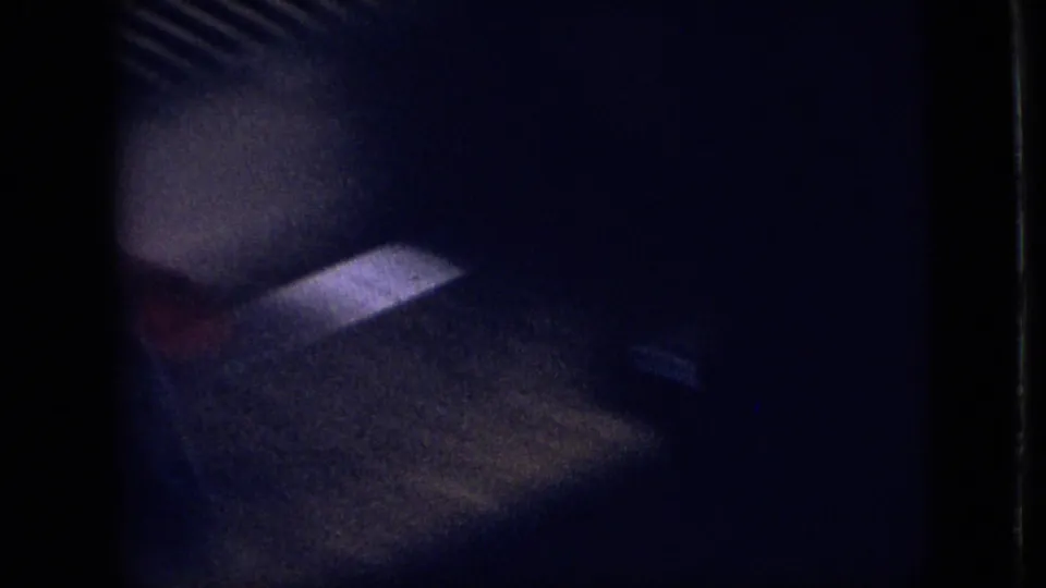 Very dark 1968 Branson 8mm frame showing a shadowed face or head near the camera, with surrounding interior or vehicle-like shadows and blue-purple grain.