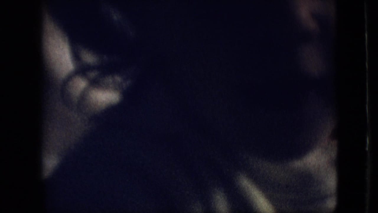 A toddler appears in a dark, grainy 1968 Branson, Missouri home-movie frame, with the face and body mostly obscured by shadow and motion blur.