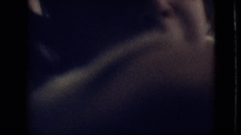A blurred toddler fills much of the dim indoor frame, with a hand or arm moving through the foreground in grainy 8mm footage from the 1968 home movie.