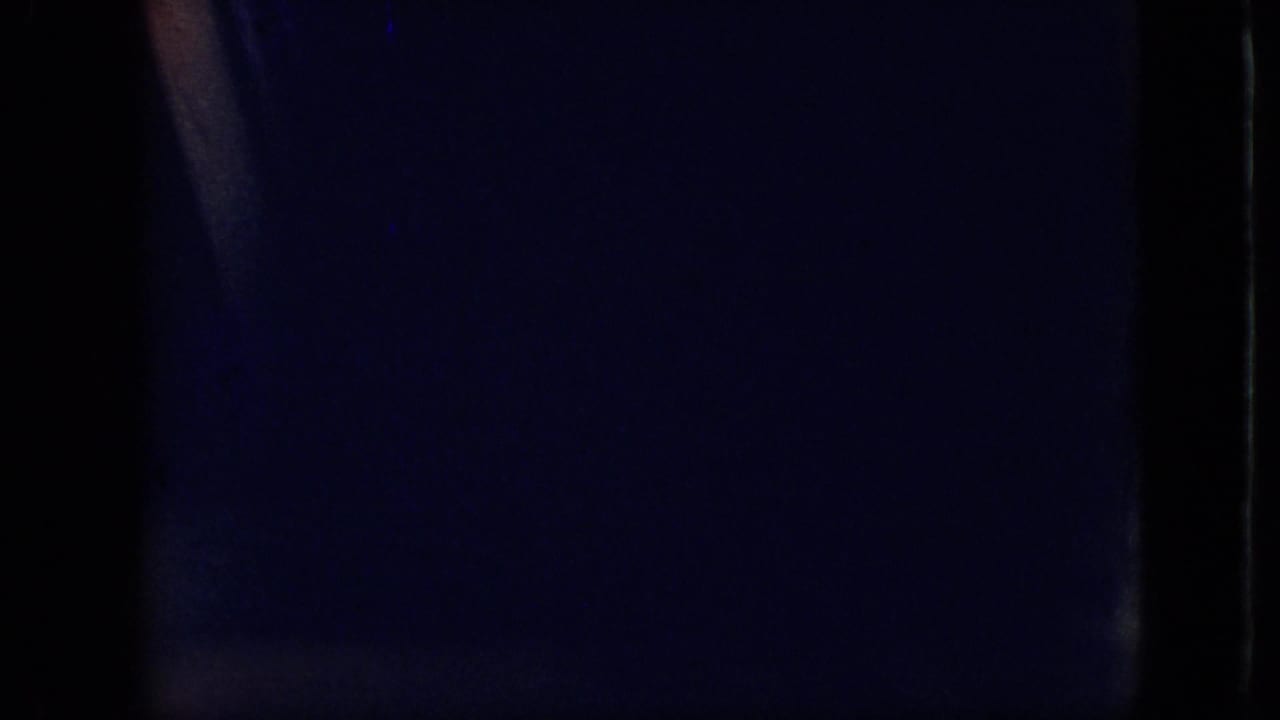 Underexposed 1968 8mm frame from the Branson, Missouri clip showing a mostly dark vehicle interior with faint blue and orange light along the film edge.