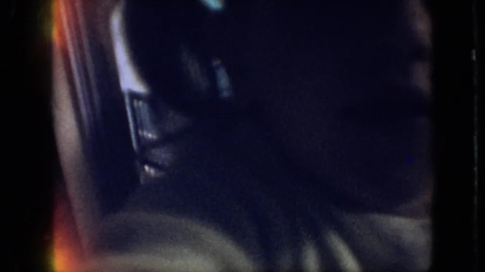 Low-light 1968 8mm frame from the Branson, Missouri clip showing a partially visible woman in close-up inside a vehicle, with dark shadows and colored film flare.