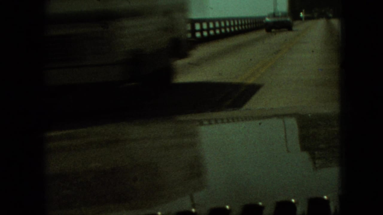 Bridge roadway seen through a dark film frame with railing and a vehicle ahead.