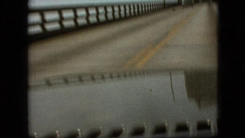1968 Branson, Missouri home-movie frame showing the bridge deck and railing from a moving car, with the yellow center line and film-frame border visible.