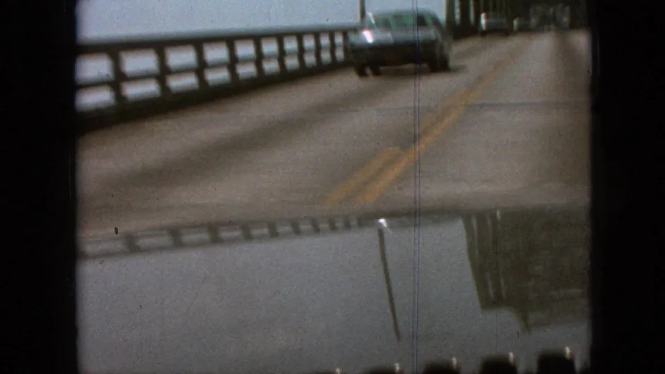 1968 Branson, Missouri frame showing a car passing on a two-lane bridge road with a side railing, yellow center stripe, and visible 8mm film borders.