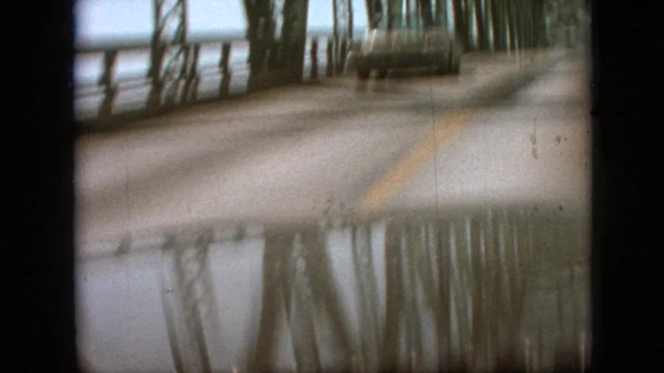 1968 vacation footage from Branson, Missouri showing a blurred oncoming car on a wet steel truss bridge, framed by the vehicle interior and film borders.