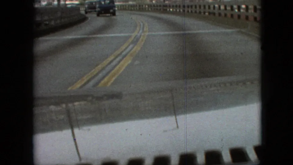 The final frame shows the car continuing along a two-way bridge road with a distant vehicle ahead, double yellow lines, railings, and visible 8mm scan borders.