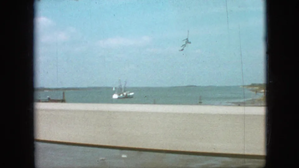 Recorded 1968 travel footage shows open water, distant shoreline, bridge railing, and a small vessel or structure seen from the moving vehicle.