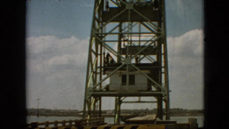 1968 home-movie frame from Branson, Missouri showing the raised steel bridge structure, control cabin, roadway barrier, waterline, distant shore, and small figures near the tower.