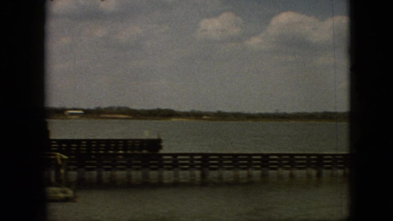 1968 Branson, Missouri home-movie frame showing a wooden pier or bridge railing over calm lake water with a low shoreline in the distance.