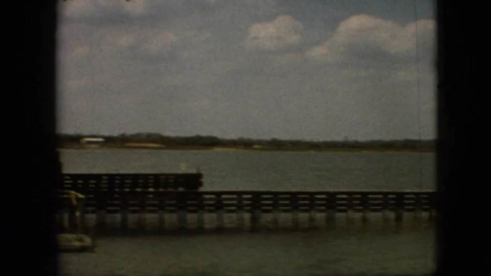 1968 Branson, Missouri home-movie frame showing a wooden pier or bridge railing over calm lake water with a low shoreline in the distance.
