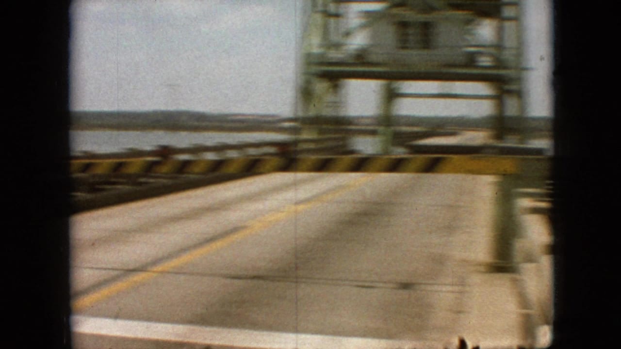 Roadway on a pier or bridge with yellow center line and water visible at the side.