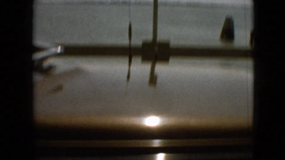 1968 8mm frame from the Missouri travel clip showing a dark passenger-window or windshield view with reflected sunlight and indistinct exterior scenery beyond the glass.