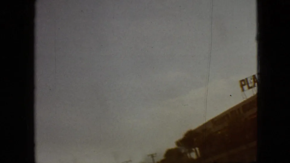 Orange-shifted 8mm frame from the same 1968 Branson road sequence, showing roadway, utility poles, and the edge of a commercial building sign.