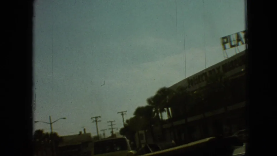 1968 Branson roadside frame with utility poles, moving cars, palm trees, and a commercial building along the right edge of the 8mm frame.