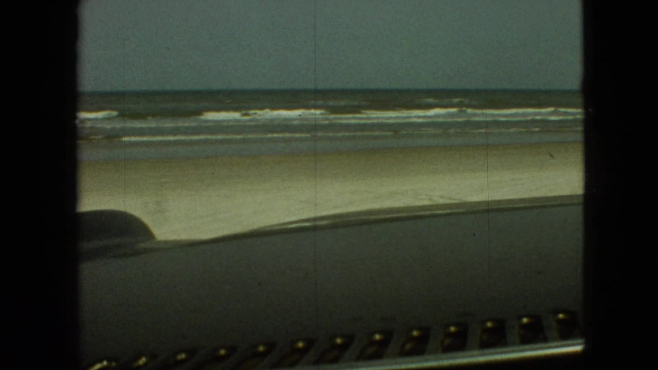 Beach and surf seen through a car windshield with the dashboard in the foreground.