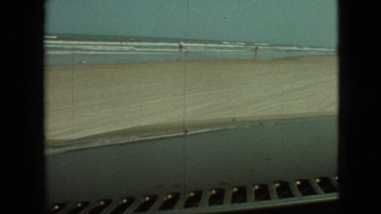 Open beach, ocean waves, and a distant figure are seen from a moving vehicle, with dashboard and film-frame edges visible in the scanned 8mm footage.