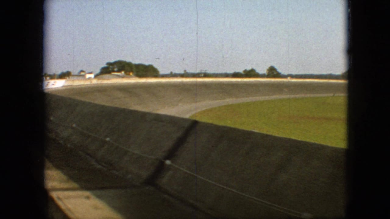 View along the curved track wall with grass and distant trees beyond the bend.
