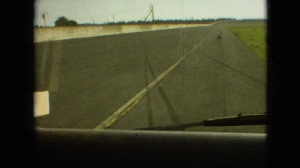 Forward-looking 8mm travel frame from inside a truck, showing the asphalt road curving along a concrete barrier with fields beyond, consistent with the supplied 1968 Missouri clip metadata.