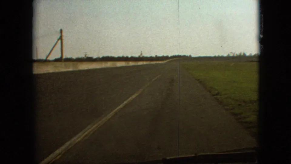 Final 1968 8mm frame from the Branson, Missouri road sequence, showing the vehicle continuing along a straight rural road beside fields and utility poles.
