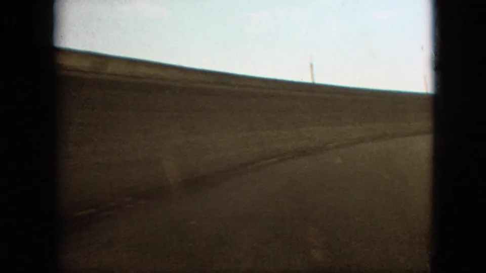 1968 Branson, Missouri home-movie frame showing a close, low-angle view of the race track surface and horizon through pronounced dark film borders.