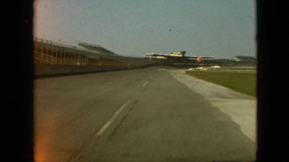 1968 Branson, Missouri 8mm frame showing a soft forward view down the paved lane, with a building-like structure at left and grass at right.