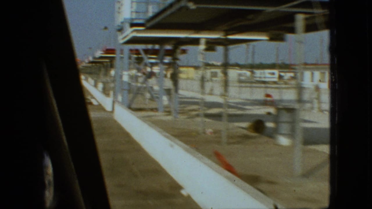 Covered walkway and open paved area with railings and low structures beside a stadium complex.