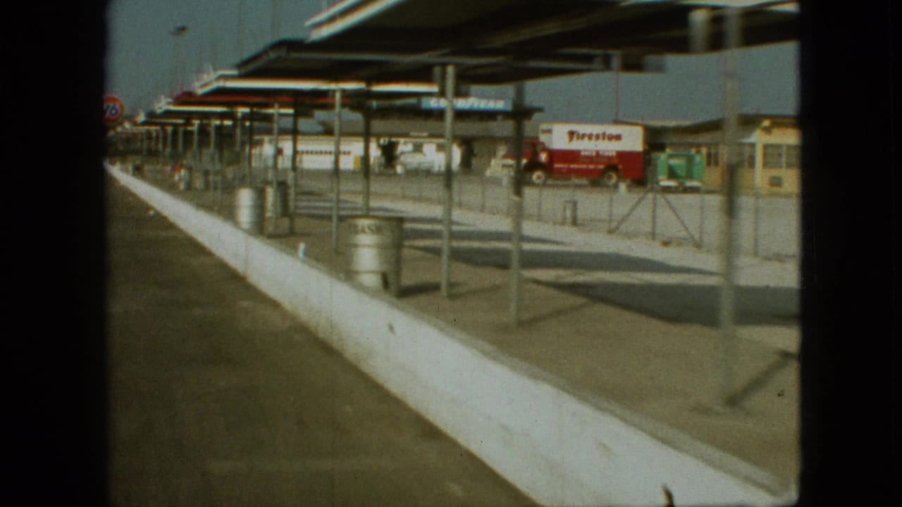 Angled view along the station canopy and barrier with a Firestone truck parked near service buildings.