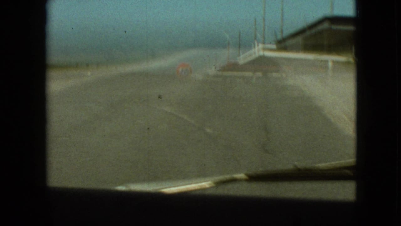Branson, Missouri 1968 home-movie frame looking through a car windshield toward a road and distant tunnel approach, with heavy softness and road glare.