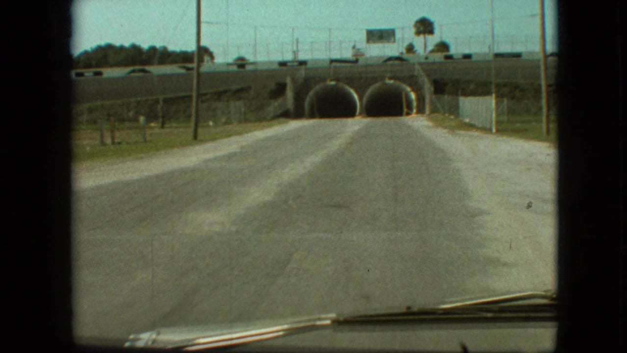 Roadway approaches two dark tunnel openings beneath an overpass.