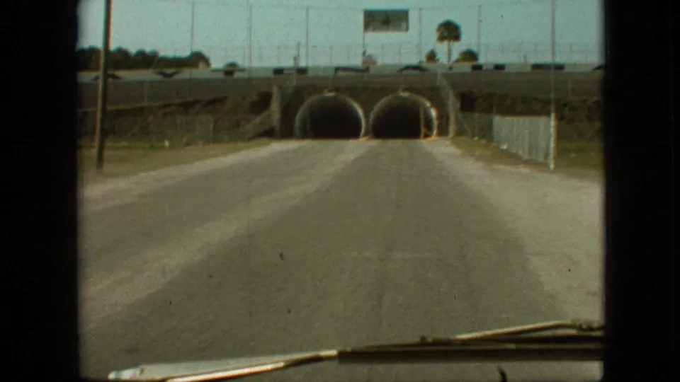 Branson, Missouri 1968 home-movie frame showing a closer approach to twin tunnel openings, with a roadside fence, overpass, sign, and windshield wiper visible.