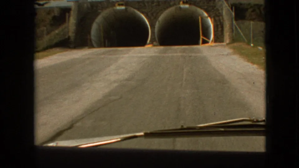 The car moves closer to the twin circular tunnel mouths beneath a stone-faced overpass in Branson, Missouri, in 1968 footage.