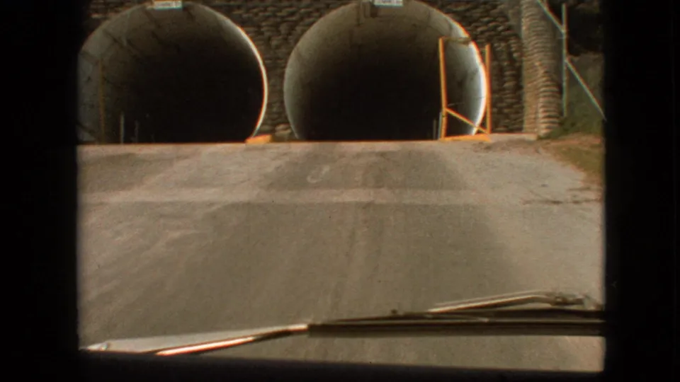 A closer 8mm frame shows the car nearly at the dual tunnel underpass, with the road rising slightly toward the dark openings.