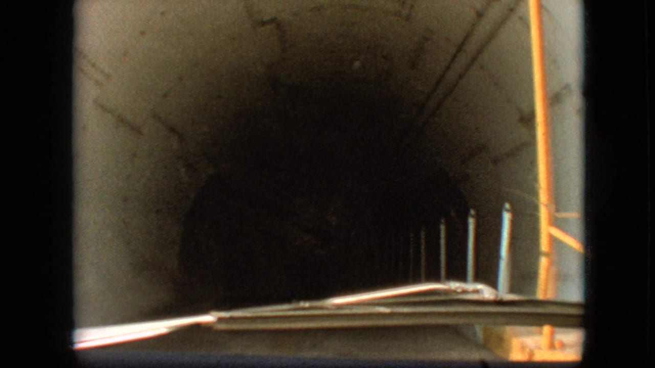 1968 8mm car POV in Branson, Missouri, looking through a dark concrete tunnel with roadside posts, a windshield edge, and light near the exit.