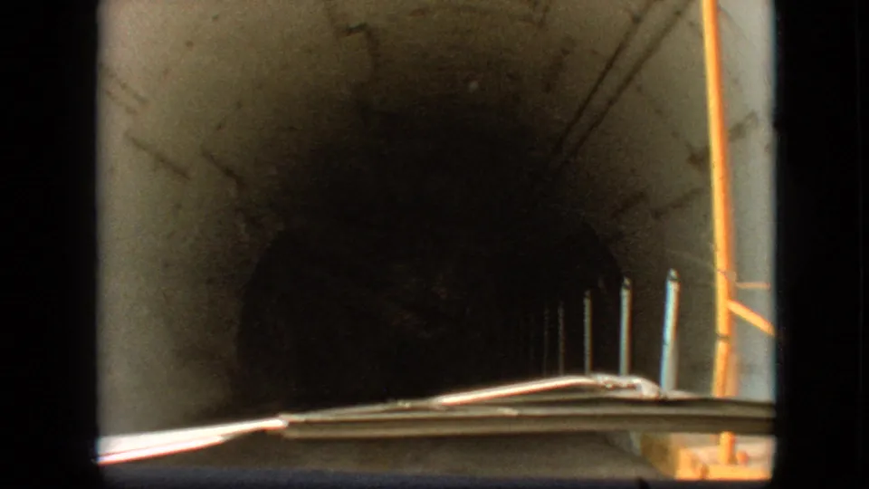 1968 8mm car POV in Branson, Missouri, looking through a dark concrete tunnel with roadside posts, a windshield edge, and light near the exit.