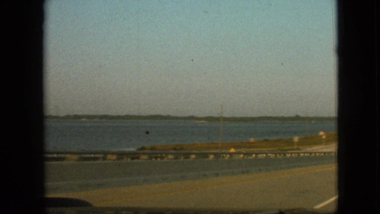 1968 8mm home-movie view near Branson, Missouri, showing a highway beside open water from inside a moving car.