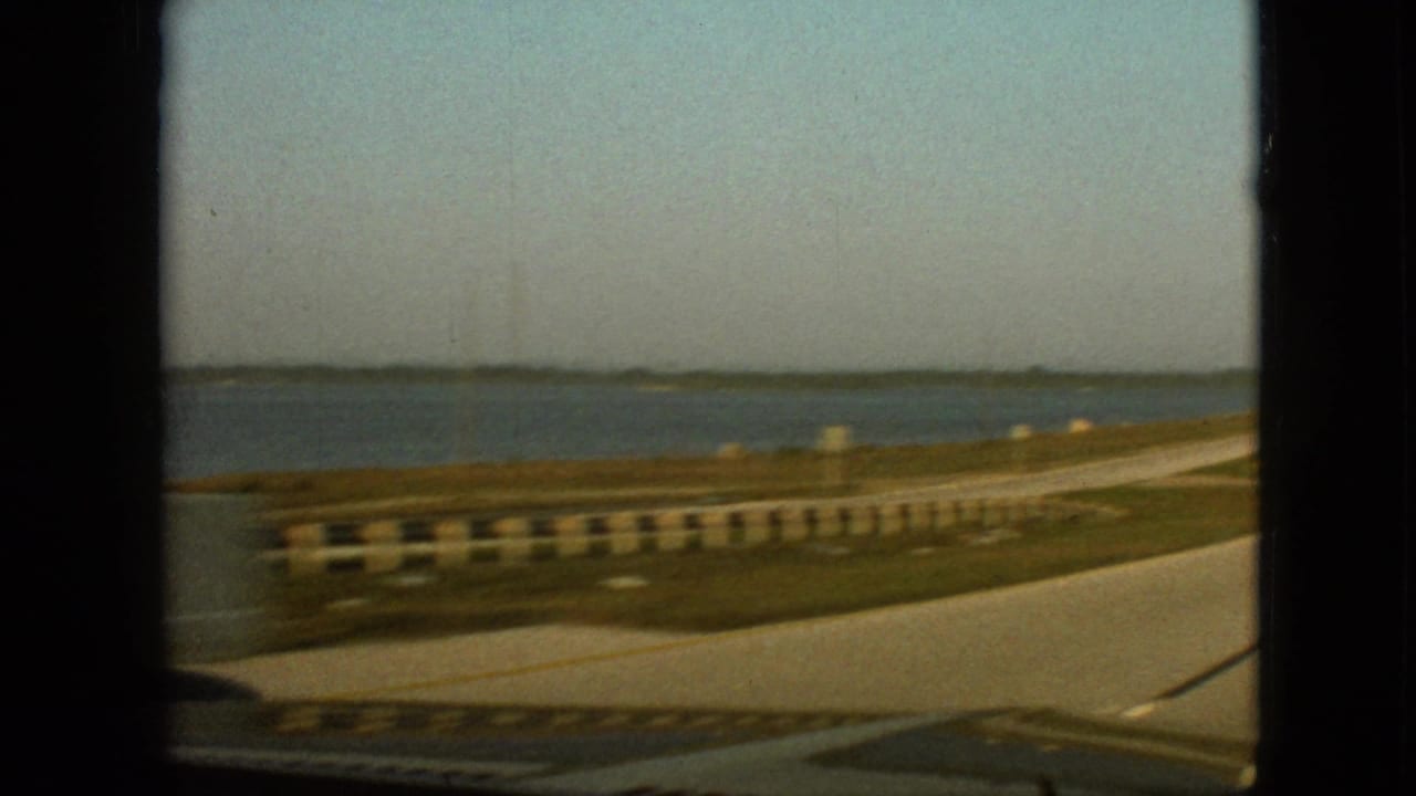 Passenger-side 8mm view of a waterside roadway near Branson, Missouri, with guardrails, grassy shoulder, and open water in the distance.