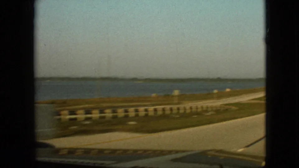 Passenger-side 8mm view of a waterside roadway near Branson, Missouri, with guardrails, grassy shoulder, and open water in the distance.