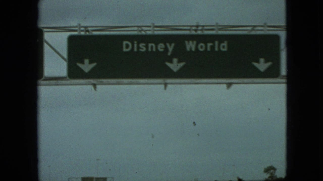 1968 8mm home-movie frame showing a green overhead Disney World highway sign through a moving car window, with dark film edges and soft focus.