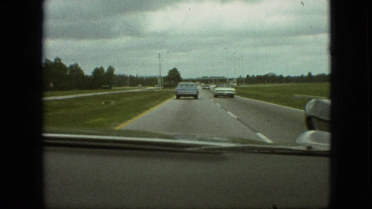 Windshield view of cars moving along a divided highway under a cloudy sky.
