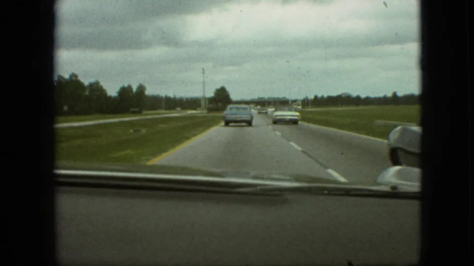 1968 Branson, Missouri road-trip footage from inside a moving car, with several vehicles ahead on a divided highway bordered by grass and trees.
