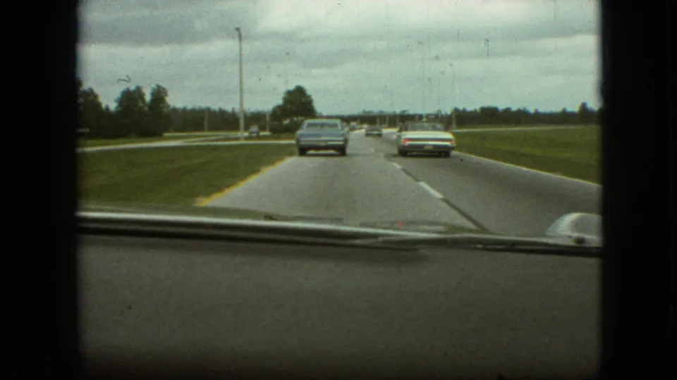 End frame from a 1968 Branson, Missouri in-car home movie, showing two automobiles ahead on a broad highway beneath heavy cloud cover.